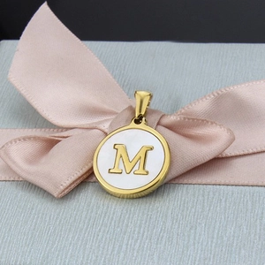 Pendentif rond doré en nacre avec lettre M sur fond de ruban en soie rose élégant