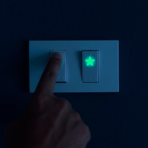 Luminous star sticker glowing green on a white light switch in a dark room environment