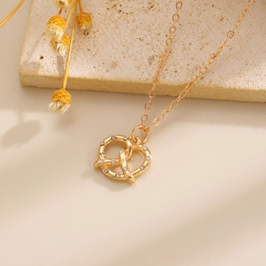 Elegante collana con ciondolo pretzel d'oro e zirconi su uno sfondo caldo e materico