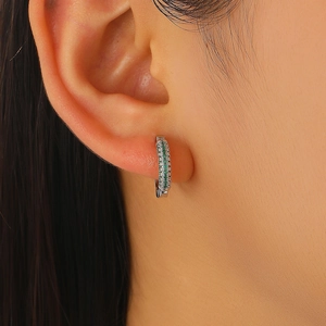 Close-up of luxury huggie earrings featuring green emerald stones and silver crystals
