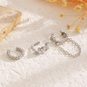 Vista de detalle de tres ear cuffs plateados con cadena y circonitas sobre piedra