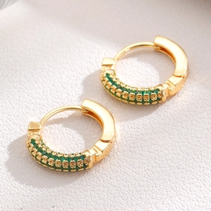 Macro detail of luxury gold hoop earrings with emerald green cubic zirconia inlay