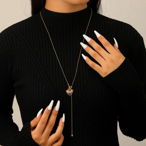 Close-up of a long gold tassel necklace with a brown resin pendant on a black sweater