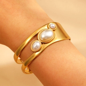 Close-up of gold-plated open bangle with three white pearls and镂空 design on wrist