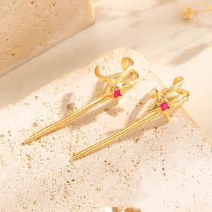 Detailansicht goldener Sternohrringe mit roten Zirkonsteinen auf Natursteinhintergrund