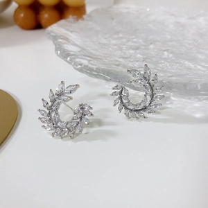 Close-up of silver C-shaped wreath earrings with marquise-cut zircons on a glass plate