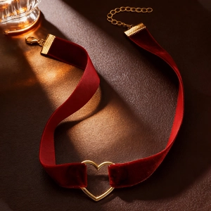 Close-up of burgundy velvet choker with a gold hollow heart pendant on leather surface