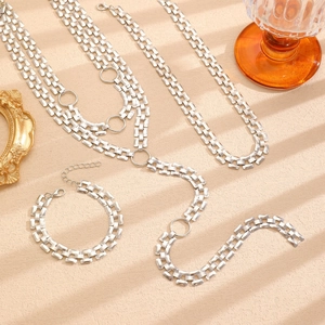 Macro shot of silver layered chain necklaces and bracelet on a textured beige surface