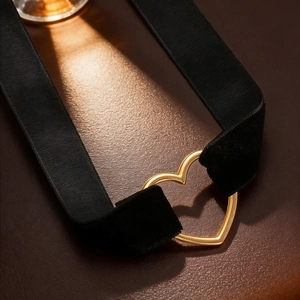 Close-up of black velvet choker with a gold hollow heart pendant on leather background