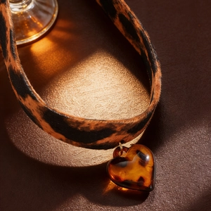 Detail of leopard print velvet choker with amber-colored heart pendant on leather