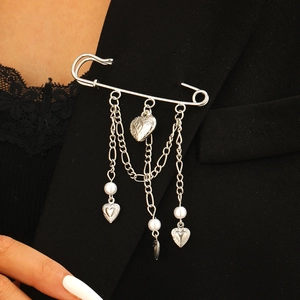 Détail d'une broche épingle argentée avec charms cœur et chaînes sur un blazer noir élégant