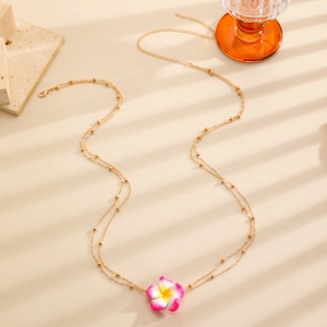 Macro detail of golden bead waist chain featuring a pink and white plumeria flower pendant