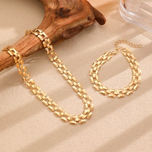 Minimalist gold necklace and bracelet set displayed on a rustic wood branch