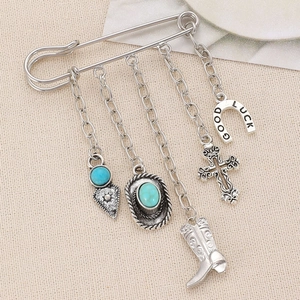 Detailed close-up of a silver Western brooch with turquoise heart and lucky horseshoe charms