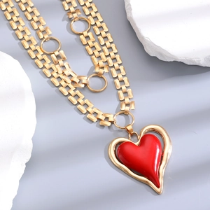 Detail of layered gold link chain necklace with a hollow heart and red enamel pendant