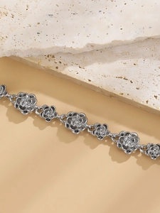 Macro shot of silver metal rose flower link bracelet on a minimalist textured stone background