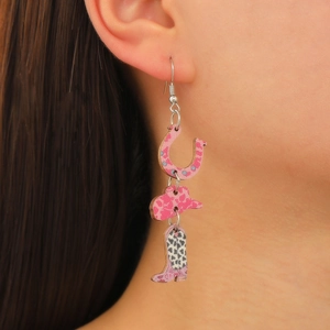 Détail de boucles d'oreilles cowboy roses avec fers à cheval, chapeaux et bottes sur modèle