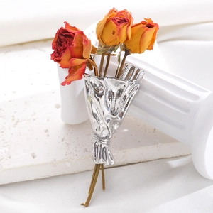 Silver flower bouquet brooch with red dried roses on a white decorative pillar