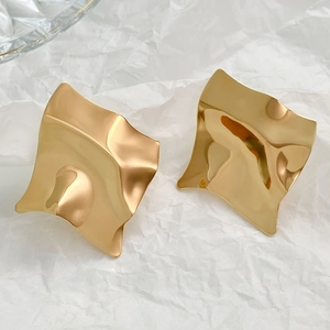 Detail of gold square earrings with irregular fluid ripples on a textured background