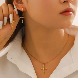Close-up of golden cross necklace and earrings set worn with a white shirt
