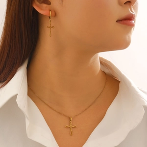 Detail of elegant gold hollow cross necklace and matching earrings set on a model