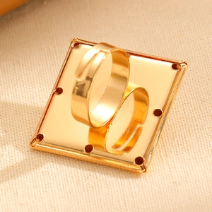 Detail of a gold geometric square ring featuring decorative edge holes and adjustable band