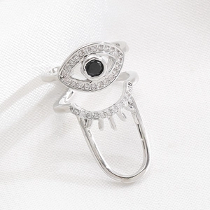 Macro shot of silver Evil Eye nail ring with white zircons on a white satin background