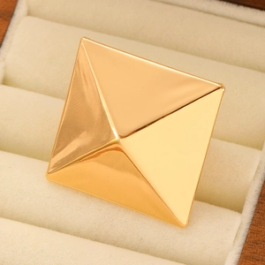 Macro shot of a geometric gold pyramid square ring on a beige velvet jewelry box