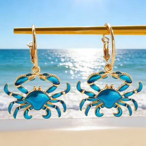 Detail shot of golden blue enamel crab earrings against a scenic summer beach background