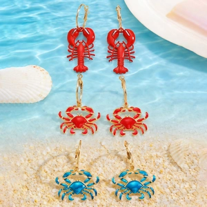 Detailed set of lobster and crab drop earrings on a beach sand background