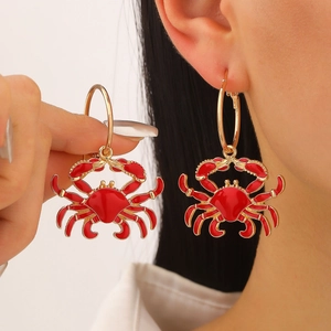 Golden hoop earrings with vibrant red enamel crab pendants in a bold beach style