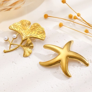 Elegant gold ginkgo leaf and starfish brooches with pearls on white marble background