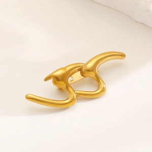Close-up of golden abstract flow brooch with matte finish on elegant beige background