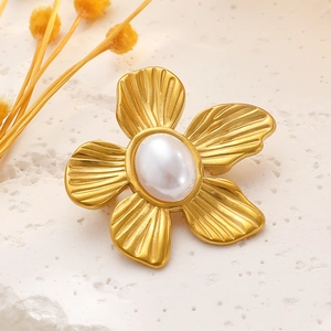 Macro detail of a matte gold flower brooch featuring a central pearl and textured petals