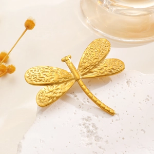 Macro detail of golden dragonfly brooch with vintage hammered metal texture on white stone