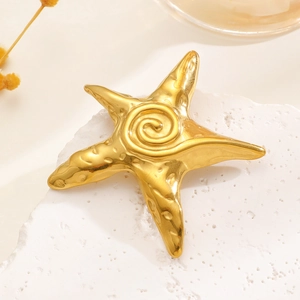 Detailed macro view of gold starfish brooch with spiral relief on a white stone surface