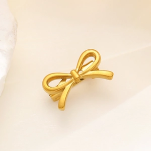 Detail of matte gold bow hair clip with secure duckbill clasp on stone background
