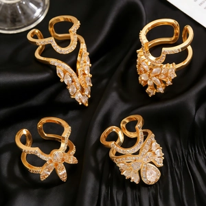 Close-up of four gold adjustable nail rings with cubic zirconia on black silk fabric