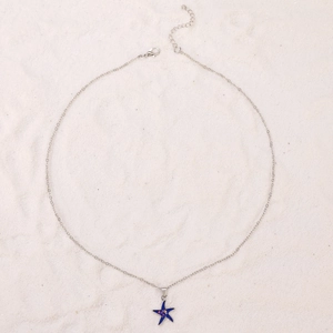 Detail of blue starfish pendant necklace with silver chain on sandy beach background