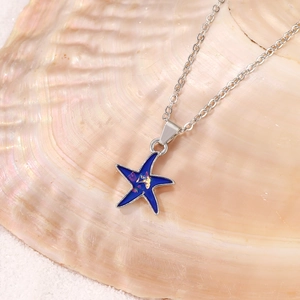 Macro detail of a blue starfish pendant with gold foil on a shell and white sand