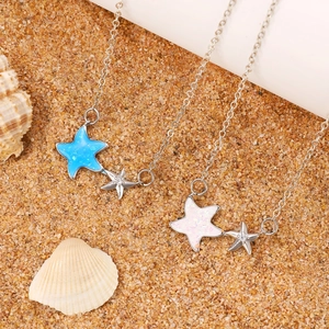 Detail of starfish pendant necklace with blue and pink sequins on a sandy beach backdrop