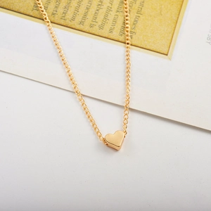 Détail d'un collier pendentif coeur 3D doré minimaliste sur un fond de magazine blanc