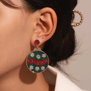 Detail of Christmas ornament earrings with green rhinestones and white snowflake patterns