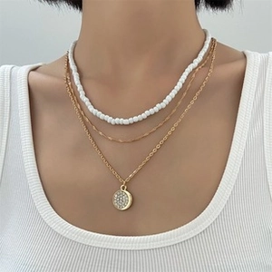 Detail van gelaagde bohemian ketting met witte kralen, gouden kettingen en kristallen hanger