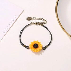 Detailed macro view of handmade yellow sunflower charm on black braided cord bracelet