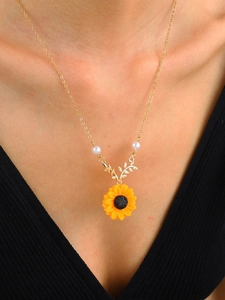 Close-up of a golden sunflower necklace with white pearls worn on a model's collarbone