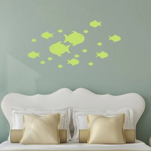 Glow in the dark fish wall decals arranged as a school over a bedroom bed headboard