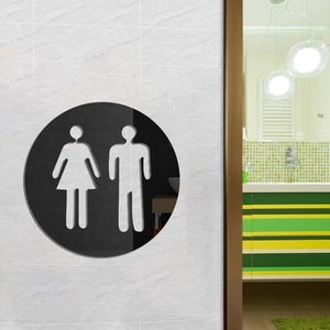 Circular black restroom sign with male and female icons on a white textured wall