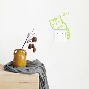 Detailed close-up of luminous green sleeping cat sticker applied over a white wall switch
