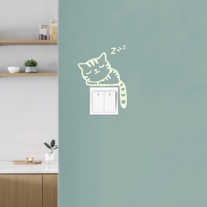 Glow-in-the-dark cat sticker sleeping above a light switch for home wall decoration